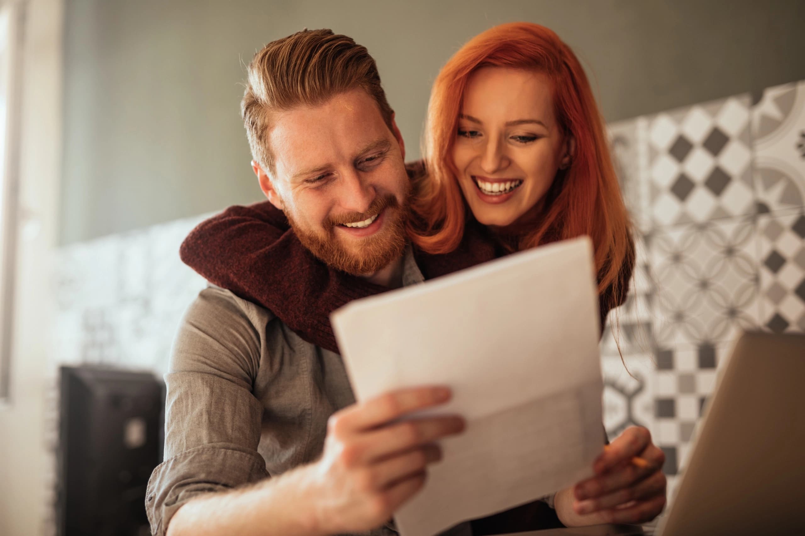 Young married couple, smiling at a finance document. The woman has her arm around her husband.